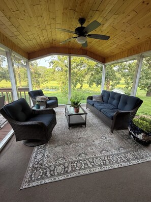 Un patio couvert aménagé avec des meubles en osier, un ventilateur de plafond et une vue sur un paysage verdoyant.