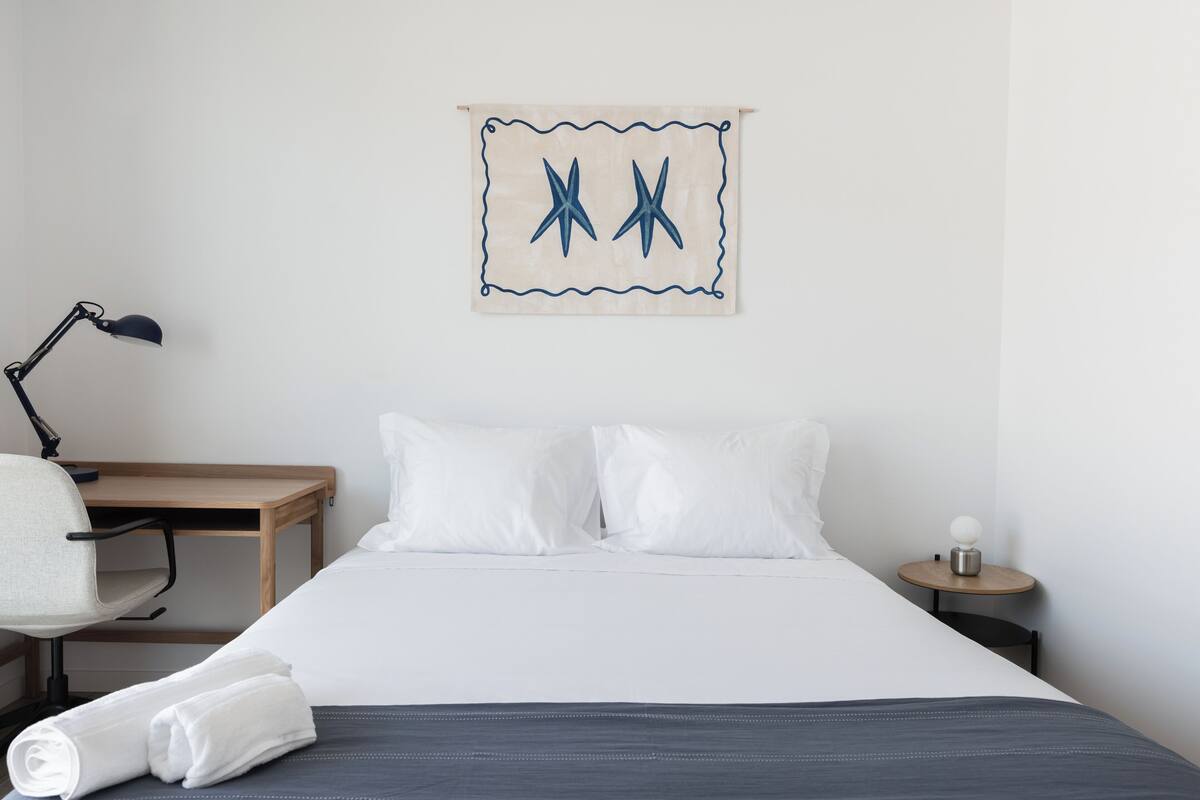 Ein ordentlich eingerichtetes Hotelzimmer mit einem Bett, einem Schreibtisch, einem Stuhl und einem Nachttisch.