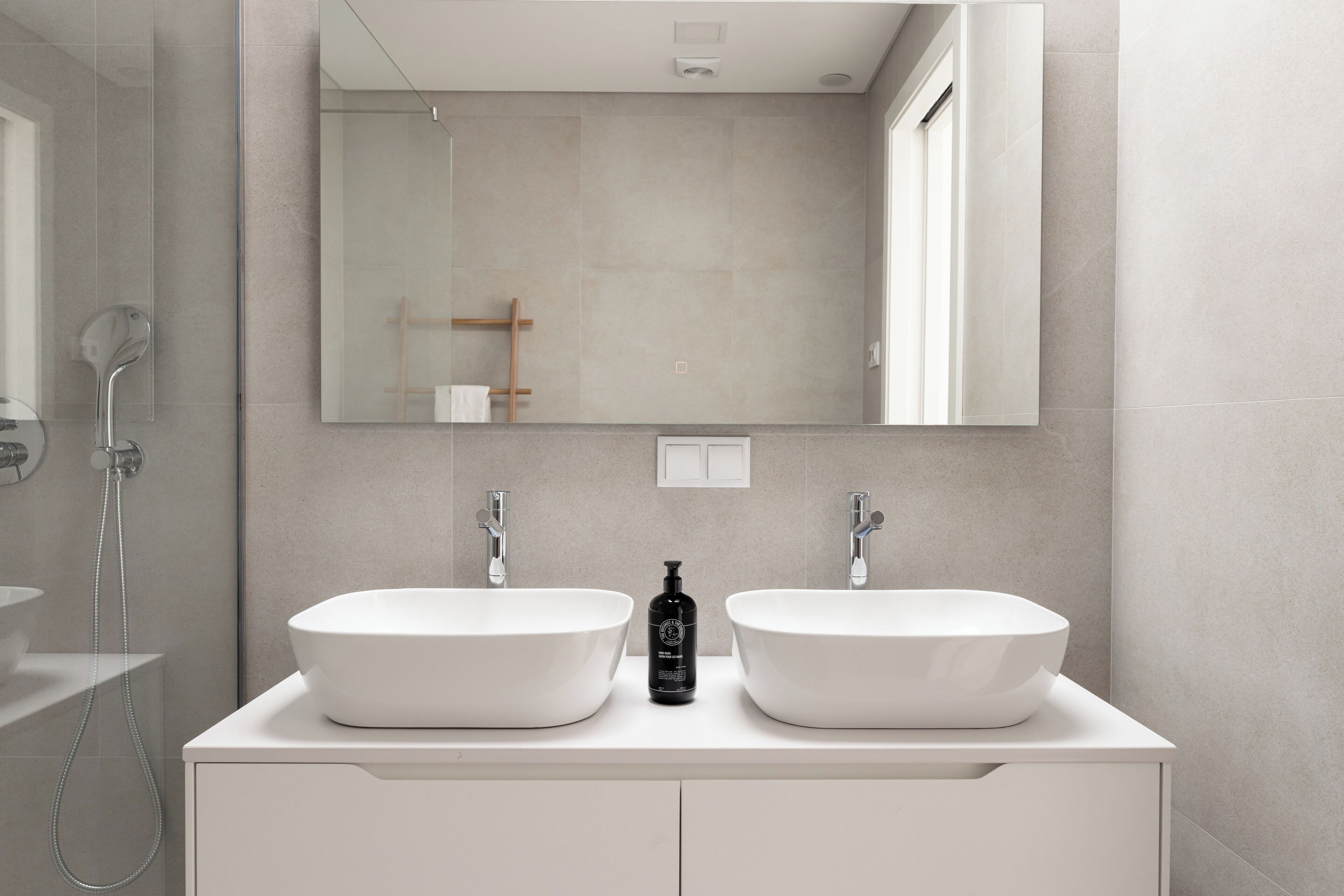 A modern bathroom with two white sinks, a large mirror, and a shower.