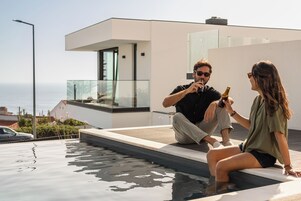 Un área de piscina moderna al aire libre con vista despejada al mar, barandilla de cristal y diseño arquitectónico minimalista.