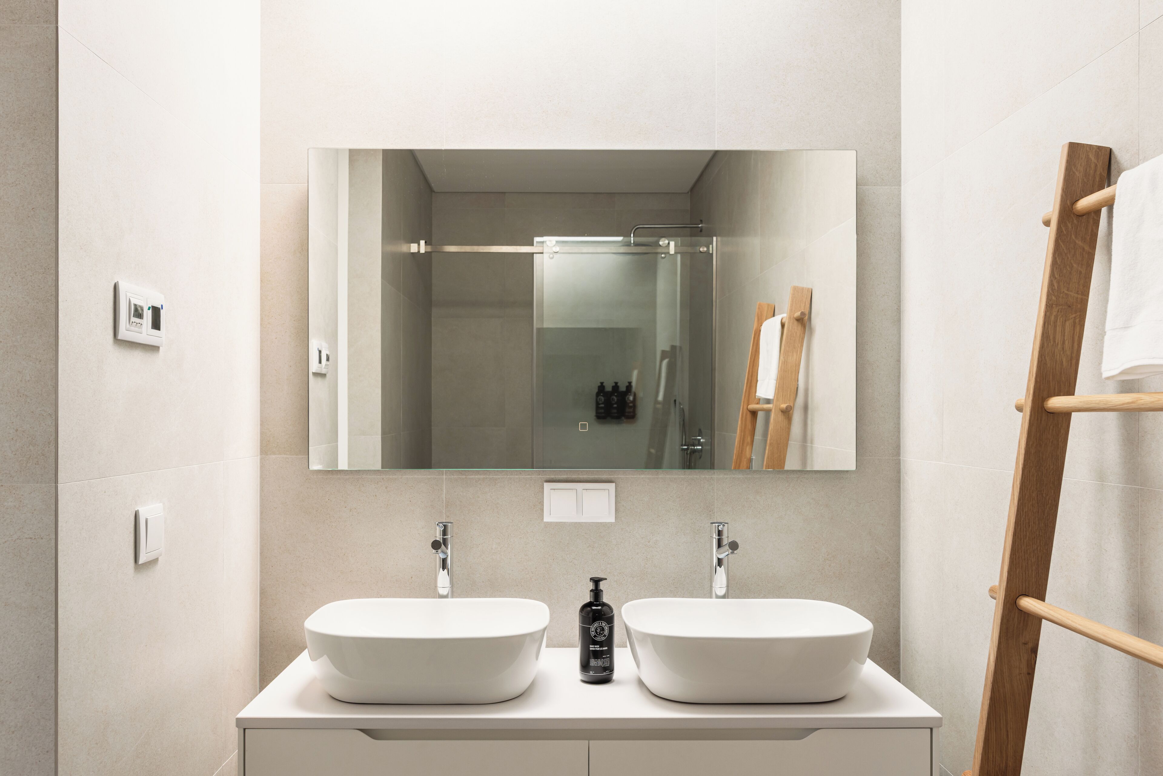 Un baño moderno con dos lavamanos blancos, un espejo grande y un toallero de madera.