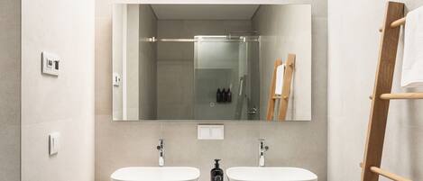 Un baño moderno con dos lavamanos blancos, un espejo grande y un toallero de madera.