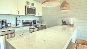Cozinha moderna com armários brancos, uma ilha grande, eletrodomésticos de aço inoxidável e luminárias pendentes de vime.
