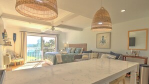 Um quarto espaçoso com uma cama grande, um espaço para sentar com uma cadeira, uma área de jantar com uma ilha de mármore e uma varanda com vista.