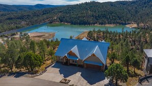 A two-story building with a blue roof, surrounded by a forested landscape and a lake. - Grindstone Lake Lodge -Views-Family Reunion Ready (Ruidoso)