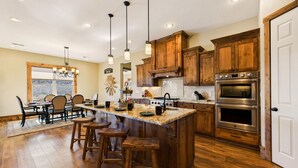 A spacious kitchen with wooden cabinets, a large island with stools, and stainless steel appliances. - Grindstone Lake Lodge -Views-Family Reunion Ready (Ruidoso)