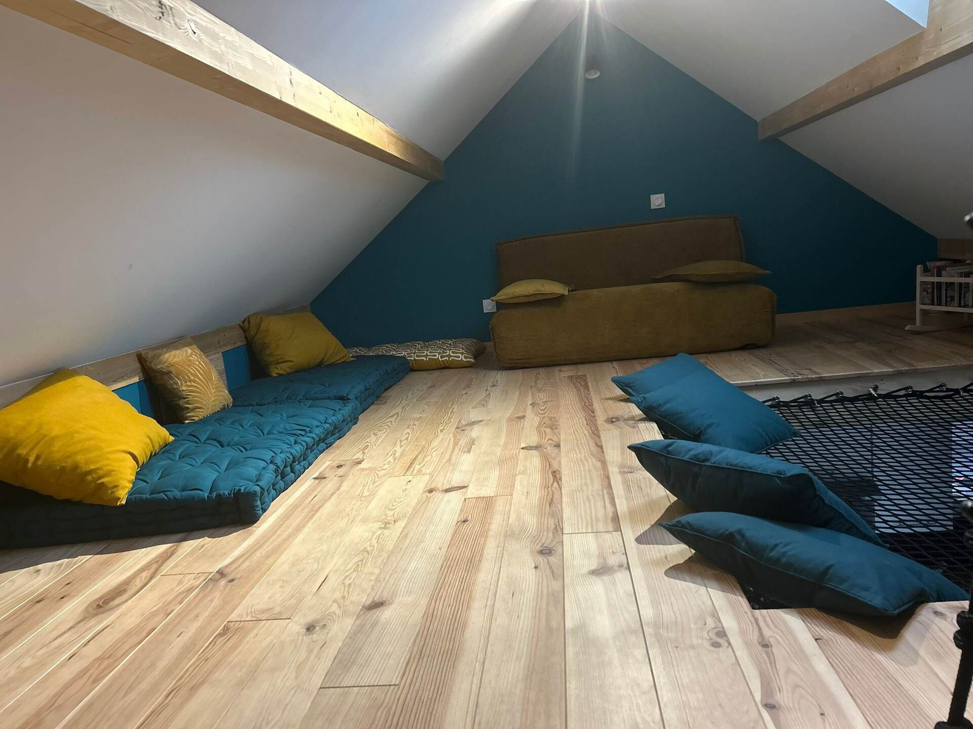 Ett sovrum på entresolplan med ett sluttande tak, träbjälkar, en blå vägg, en bäddsoffa och en hängmatta.