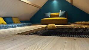A cozy attic bedroom with a sloped ceiling, a wooden floor, a bed with a black metal frame, and a blue and yellow sofa. - Gite with Spa (Arras-en-Lavedan)