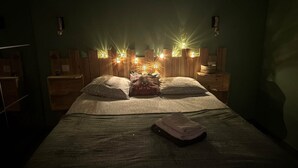 A dimly lit room with a bed, wooden headboard, and wall-mounted lights. - Gite with Spa (Arras-en-Lavedan)