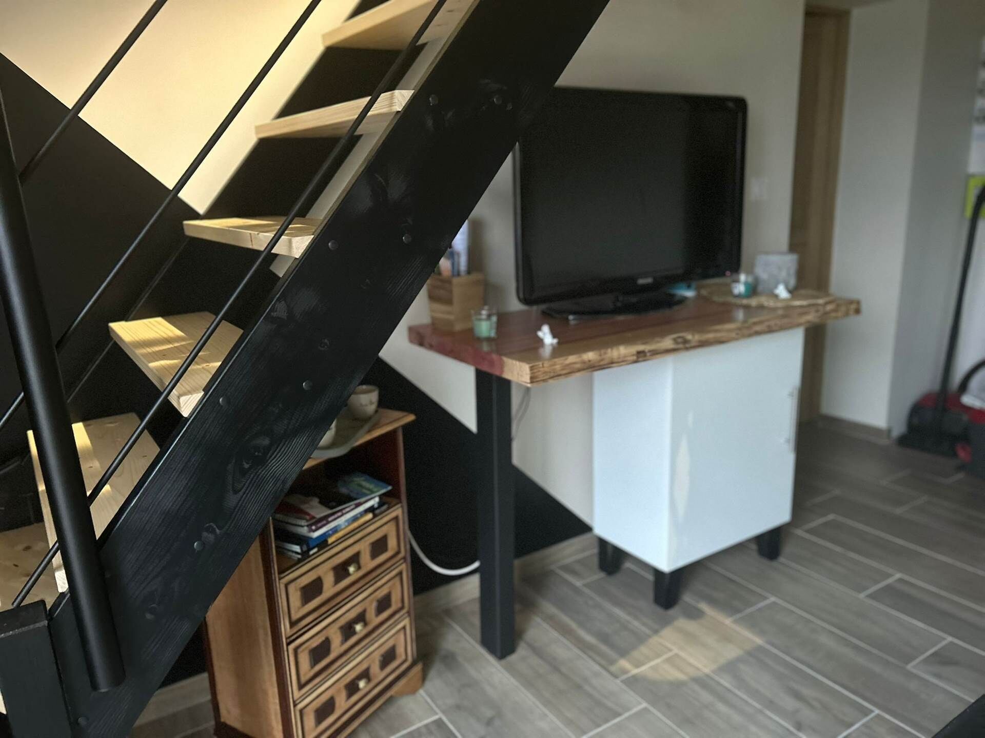 A modern living room with a staircase, a flat-screen TV, and a wooden desk.