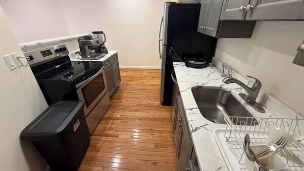 A compact kitchen with a black stove, a coffee maker, and a sink with a dish rack. - NYC Skyline Apartment (Weehawken Township)