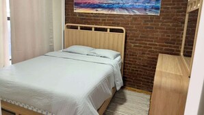 A bedroom with a wooden bed, a brick wall, and a large painting of a sunset over the ocean. - NYC Skyline Apartment (Weehawken Township)