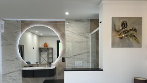 Un baño moderno con un espejo curvo, un lavamanos de mármol y una zona de ducha.