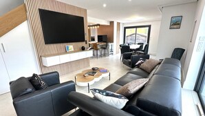 Una sala de estar moderna con un sofá de cuero negro, una mesa de centro y un televisor de pantalla plana montado en una pared de madera.
