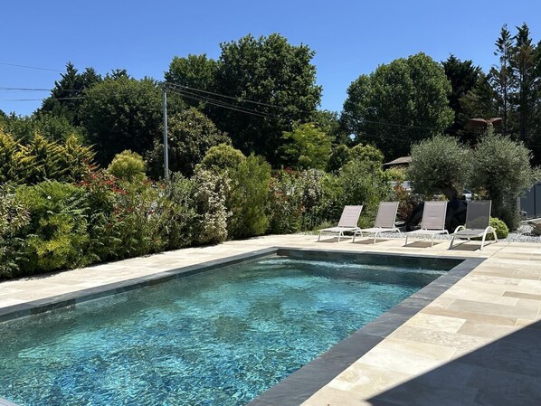 Une piscine rectangulaire à l’eau claire, entourée d’une terrasse en pierre et de chaises longues.