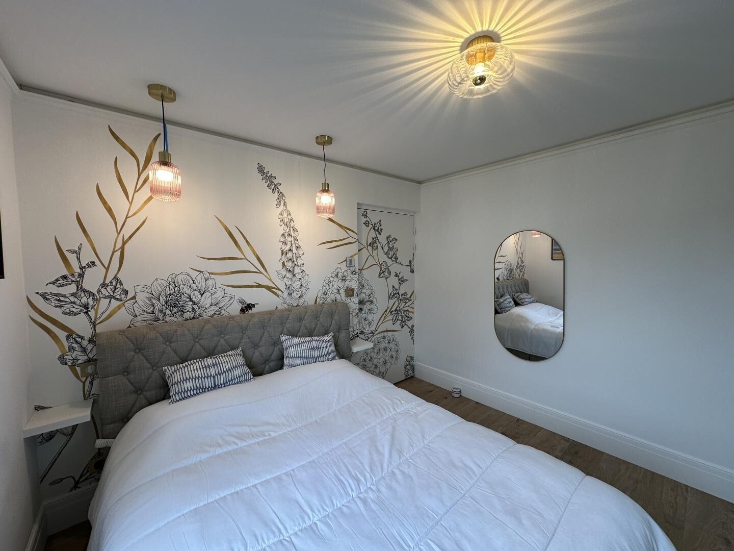 Une chambre avec un grand lit, un miroir rond et des œuvres d’art murales.