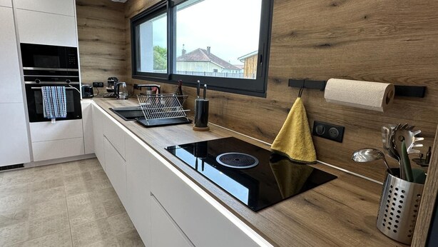 Una cocina moderna con una cocina de inducción negra, un horno integrado y un ventanal sobre el fregadero.
