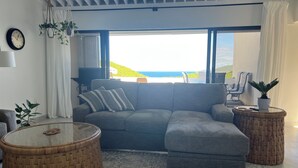 A modern living room with a grey sectional sofa, a round wooden coffee table, and a view of the ocean. - Changes in Latitude 18.3 spacious Mahogany Run condo with ocean views. (St Thomas)