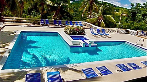 A rectangular swimming pool with a 4ft depth marker, surrounded by blue lounge chairs and palm trees. - Changes in Latitude 18.3 spacious Mahogany Run condo with ocean views. (St Thomas)