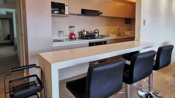 Eine moderne Küche mit Kochinsel, Barhocker und einem schwarzen Metallregal.