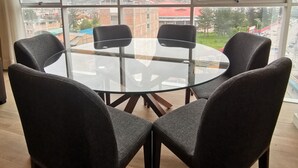 Ein Zimmer mit großem Fenster, einem runden Glastisch und vier dunklen Stühlen.