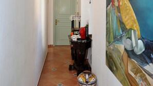 A hallway with a tiled floor, a green door, a table with a vase, and a large painting on the wall. - B&B La Cascata   Camera Amalfi (AMALFI)