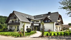 Ein zweistöckiges Gebäude mit geneigtem Dach, mehreren Balkonen und einem gepflegten Garten.