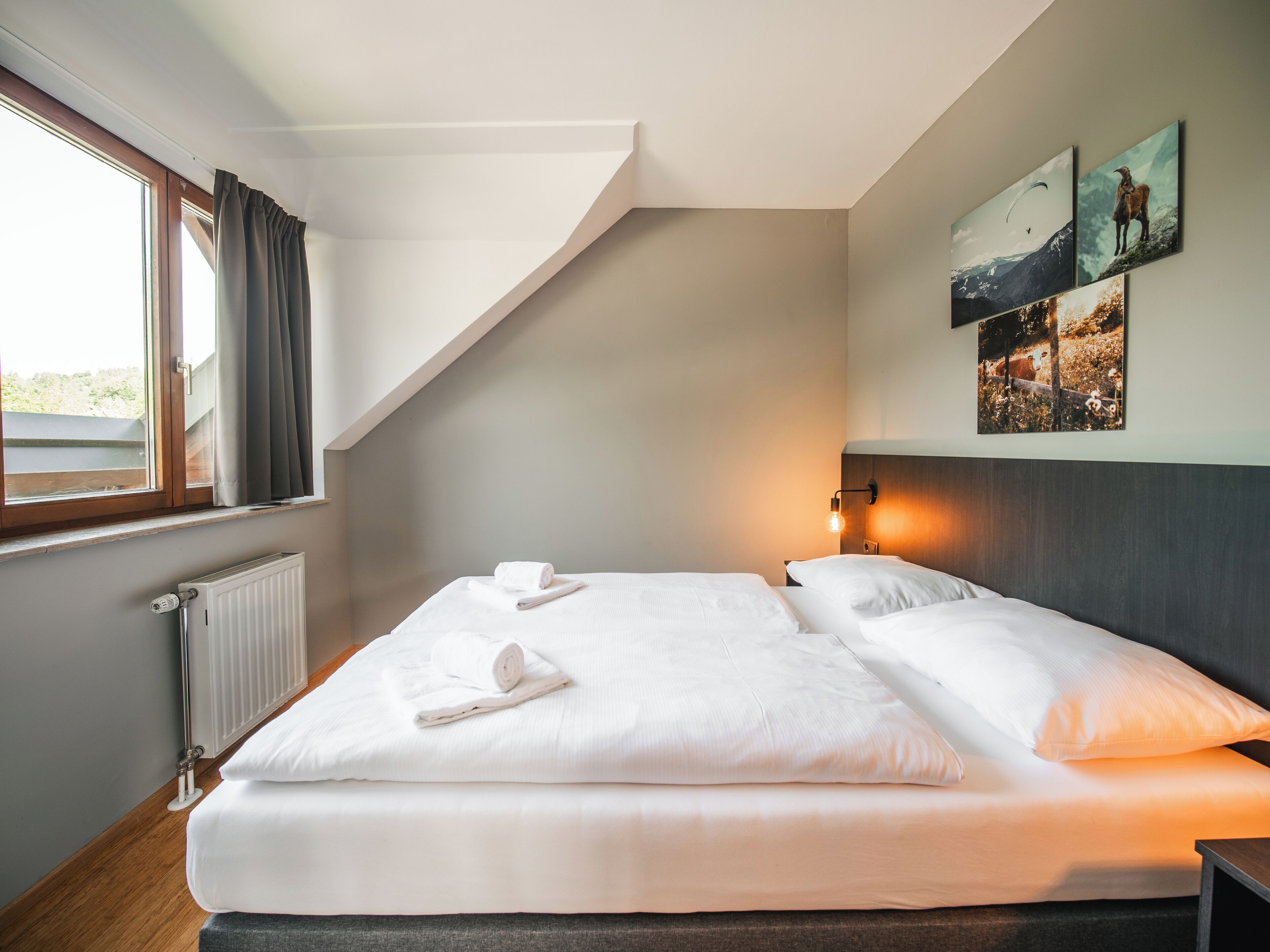 A modern hotel room with a large bed, a radiator, a window with curtains, and wall-mounted artwork.