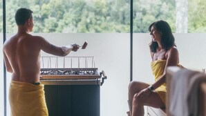Ein Mann grillt draußen, eine Frau sitzt in der Nähe.