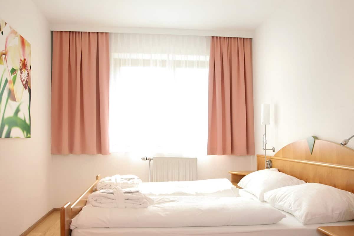 Ein ordentlich bezogenes Bett mit weißen Leinen, einem Holz-Kopfteil und einem Nachttisch mit Lampe.