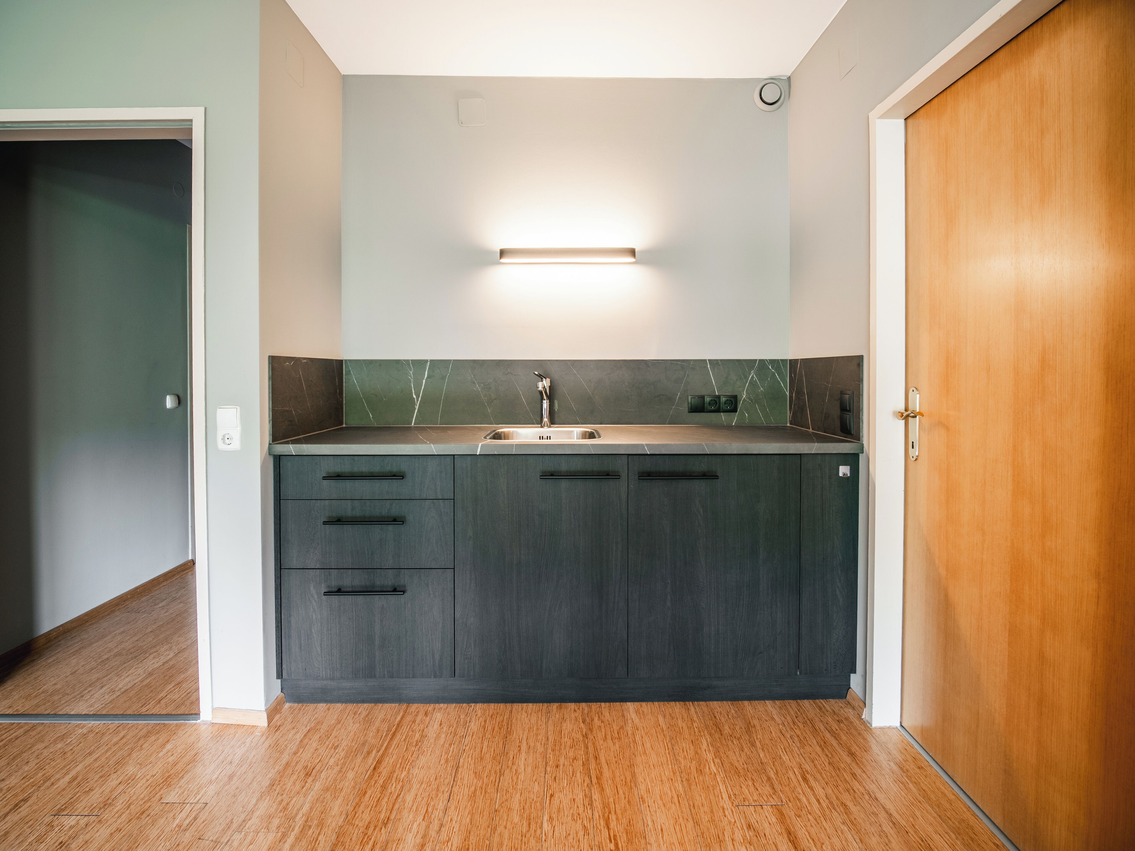 A modern kitchen with dark cabinetry, a stainless steel sink, and a light fixture above the countertop.