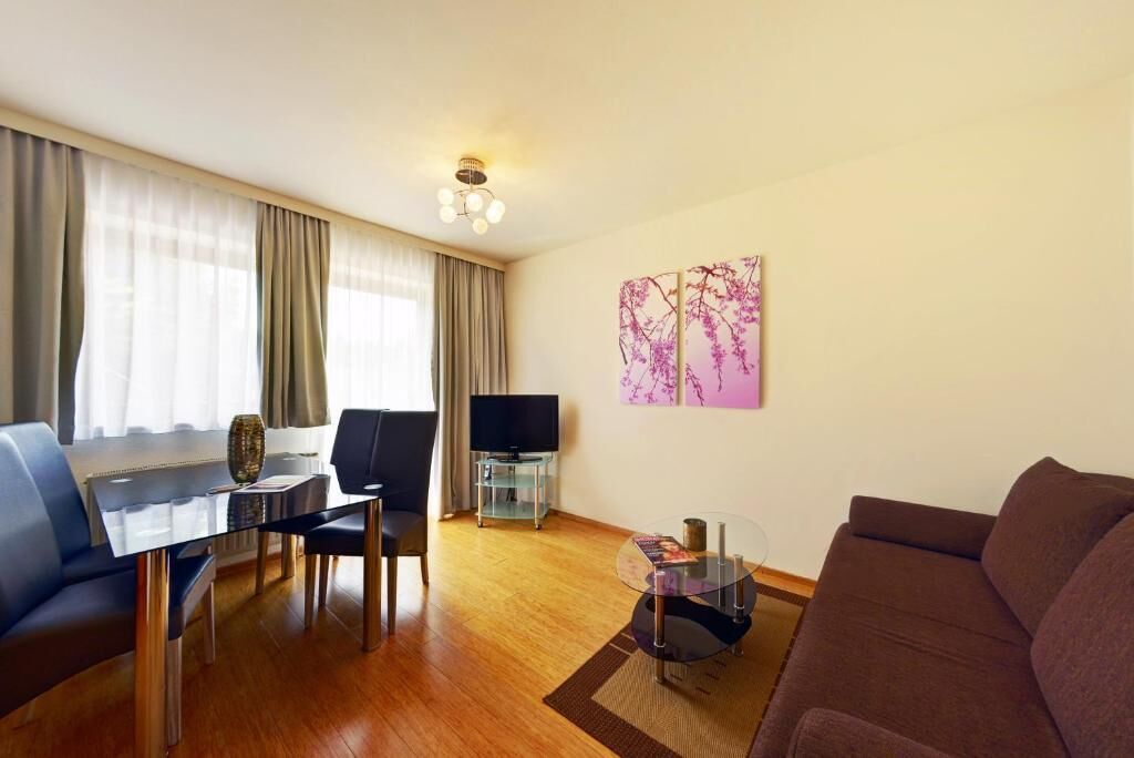 A modern living room with a glass coffee table, a sofa, a TV on a stand, and a painting on the wall.
