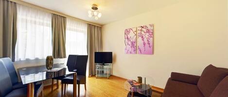 A modern living room with a glass coffee table, a sofa, a TV on a stand, and a painting on the wall.