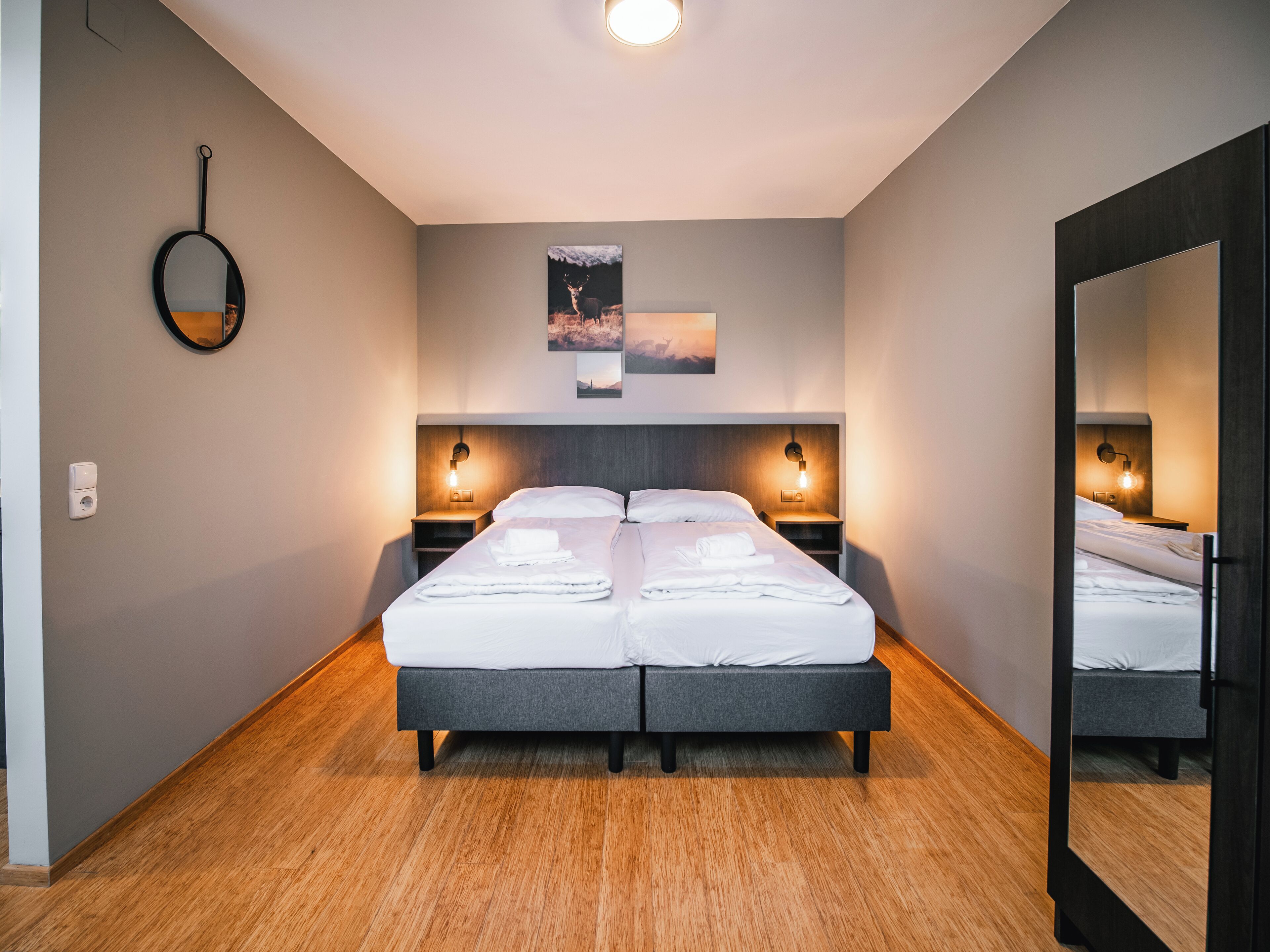 Een moderne hotelkamer met een groot bed, nachtkastjes met lampen, een spiegel en een ingelijste foto aan de muur.