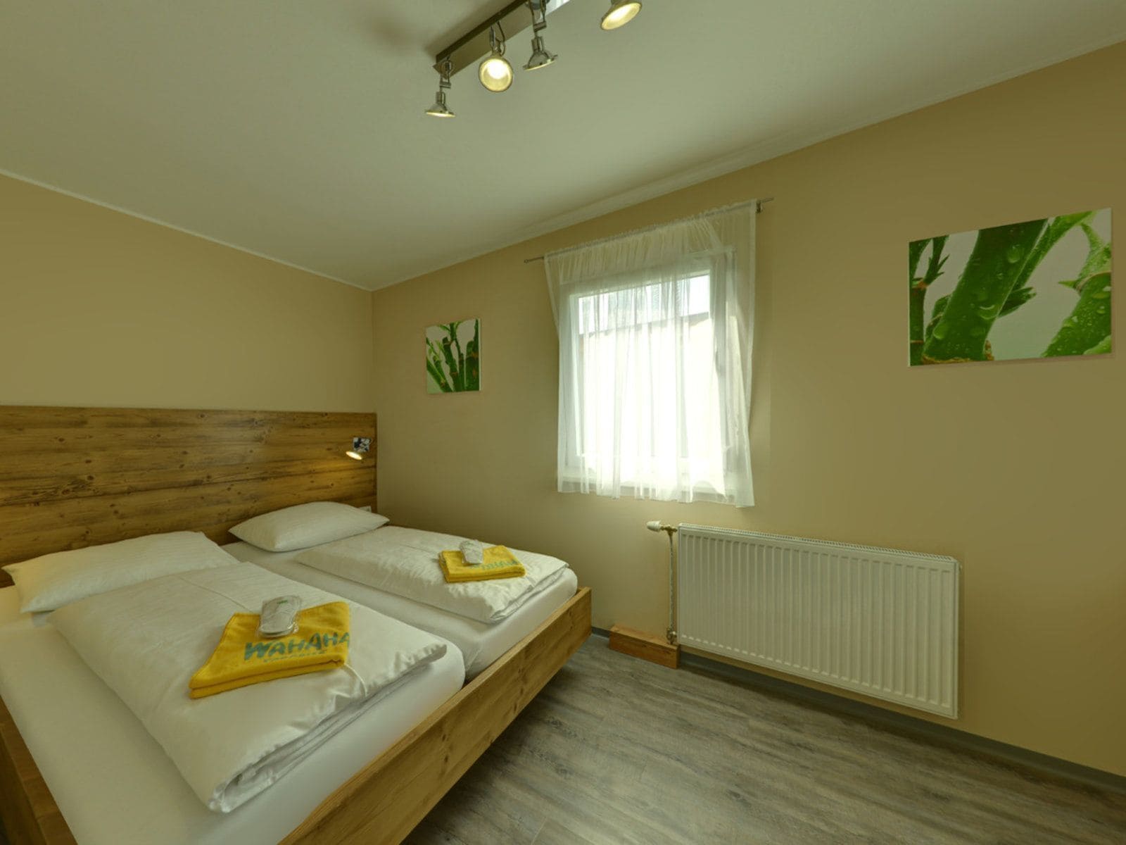 Un dormitorio con dos camas, cabeceros de madera, un radiador y una ventana con cortinas translúcidas.
