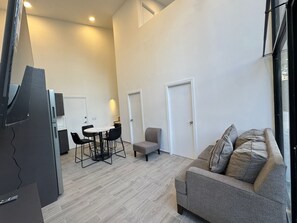 A modern living room with a grey sofa, a small table with chairs, and a TV on a stand. - Casa Di Valle (Valle de Ángeles)