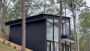 Un bâtiment moderne à deux étages, doté d’une façade noire et de grandes fenêtres en verre, entouré d’arbres.