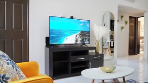 Een woonkamer met een televisie op een zwart tv-meubel, een witte ronde salontafel en een gele bank.