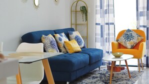 Een moderne woonkamer met een blauwe bank, een oranje fauteuil en gekleurde kussens.