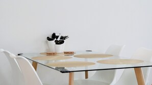 Een moderne eettafel met een glazen blad en houten poten, omringd door witte stoelen.