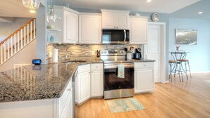 A modern kitchen with white cabinets, granite countertops, stainless steel appliances, and a dining area with a glass table and metal chairs. - Bay Avenue Bliss, Newly Updated, Spacious Yard, OCNJ South Shore (Ocean City)