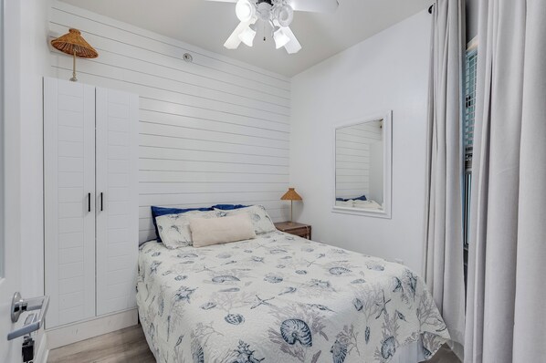 A bedroom with a bed, a wardrobe, a ceiling fan, a nightstand, and a window with curtains.