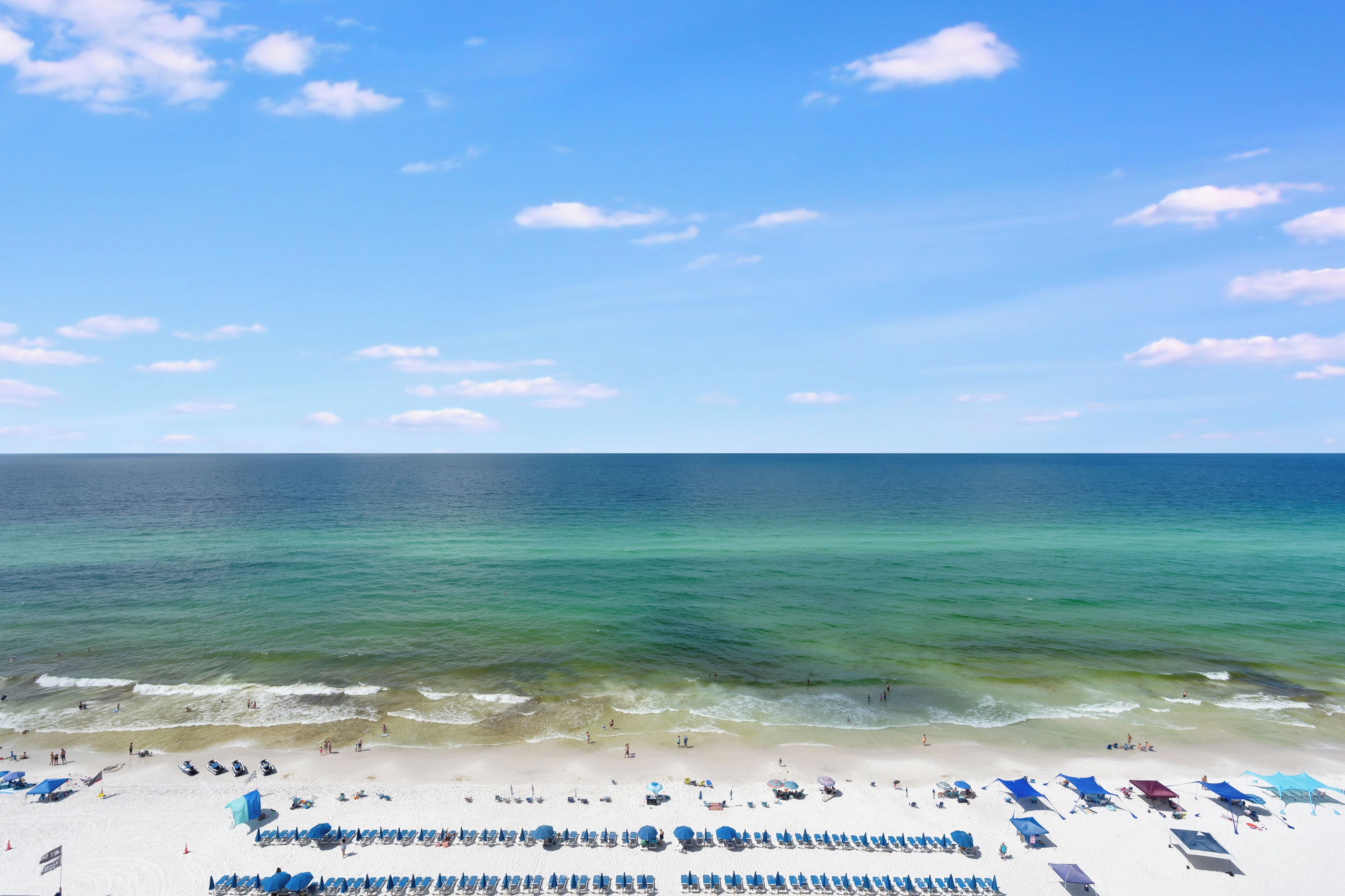 Une plage bordée de rangées de chaises longues et de parasols, un ciel dégagé et une mer calme.