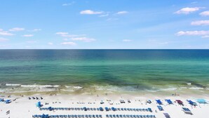 Ein Strand mit Liegestühlen und Sonnenschirmen, wolkenloser Himmel und ruhigem Meer.