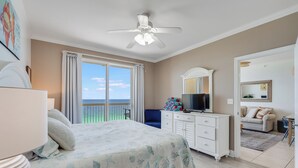 Ein Schlafzimmer mit Bett, Deckenventilator, Kommode, Fernseher und Meerblick durch eine Schiebetür.