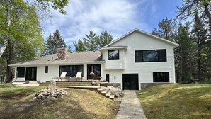 A modern two-story house with a stone chimney, a wooden deck, and a stone wall. - Lakefront Home on Crosslake - Perfect Location for Fun in the Lakes Area! (Crosslake)