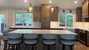 A modern kitchen with a large island, bar stools, pendant lighting, and wooden cabinets. - Lakefront Home on Crosslake - Perfect Location for Fun in the Lakes Area! (Crosslake)