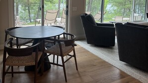 A room with a round table and chairs, a sofa, and large windows offering a view of trees and a lake. - Lakefront Home on Crosslake - Perfect Location for Fun in the Lakes Area! (Crosslake)