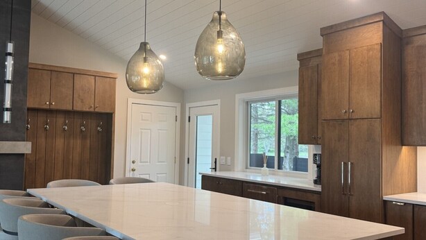 A modern kitchen with a central island, bar stools, wooden cabinets, pendant lights, and a view of the outdoors. - Lakefront Home on Crosslake - Perfect Location for Fun in the Lakes Area! (Crosslake)