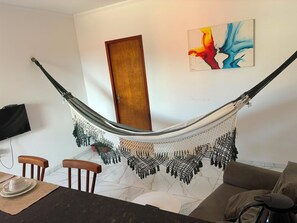 Eine Hängematze, die zwischen zwei Holztüren in einem Raum mit Marmorboden, einem Gemälde an der Wand und einem Fernseher links von ihr gespannt ist.